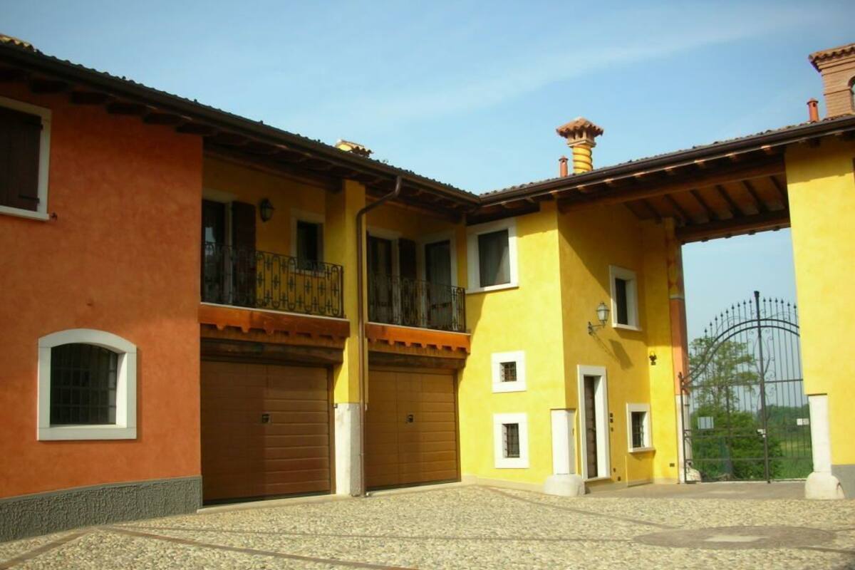 A two-story building with a yellow facade, a brown garage door, and a metal gate in the background.