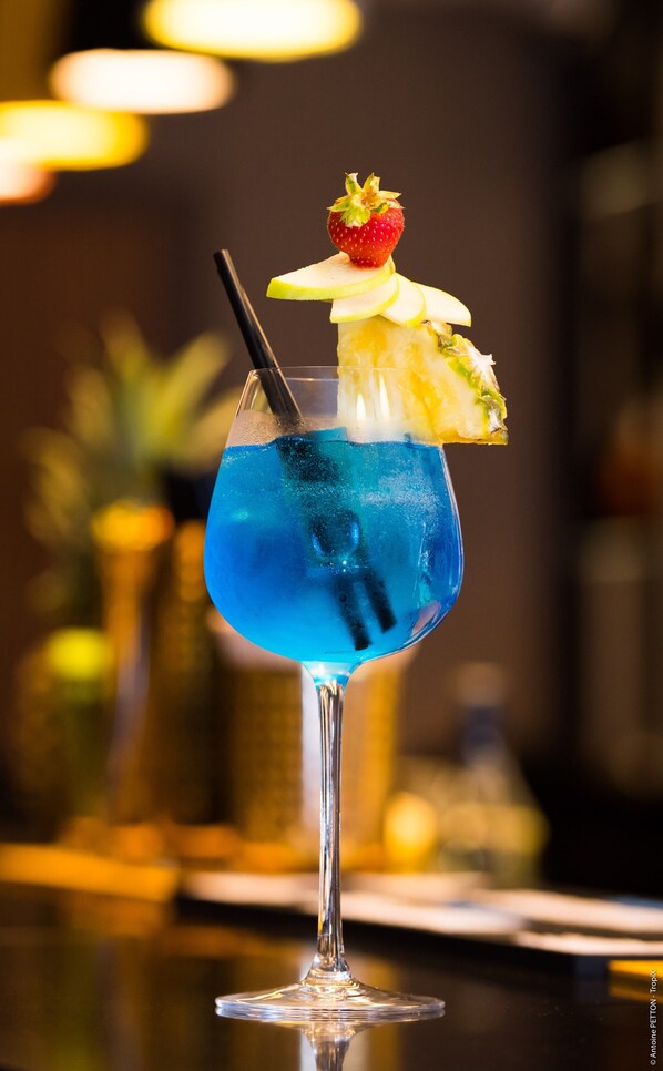 A cocktail with a blue liquid, a strawberry, and a slice of pineapple on the rim of a glass. - Simon Hotel (Fort-de-France)
