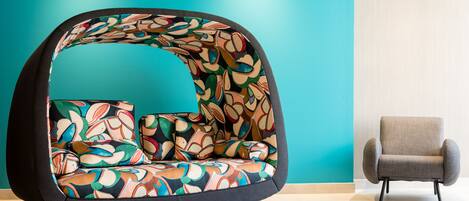 A modern room with a colorful, abstract-patterned sofa and a plain grey armchair.