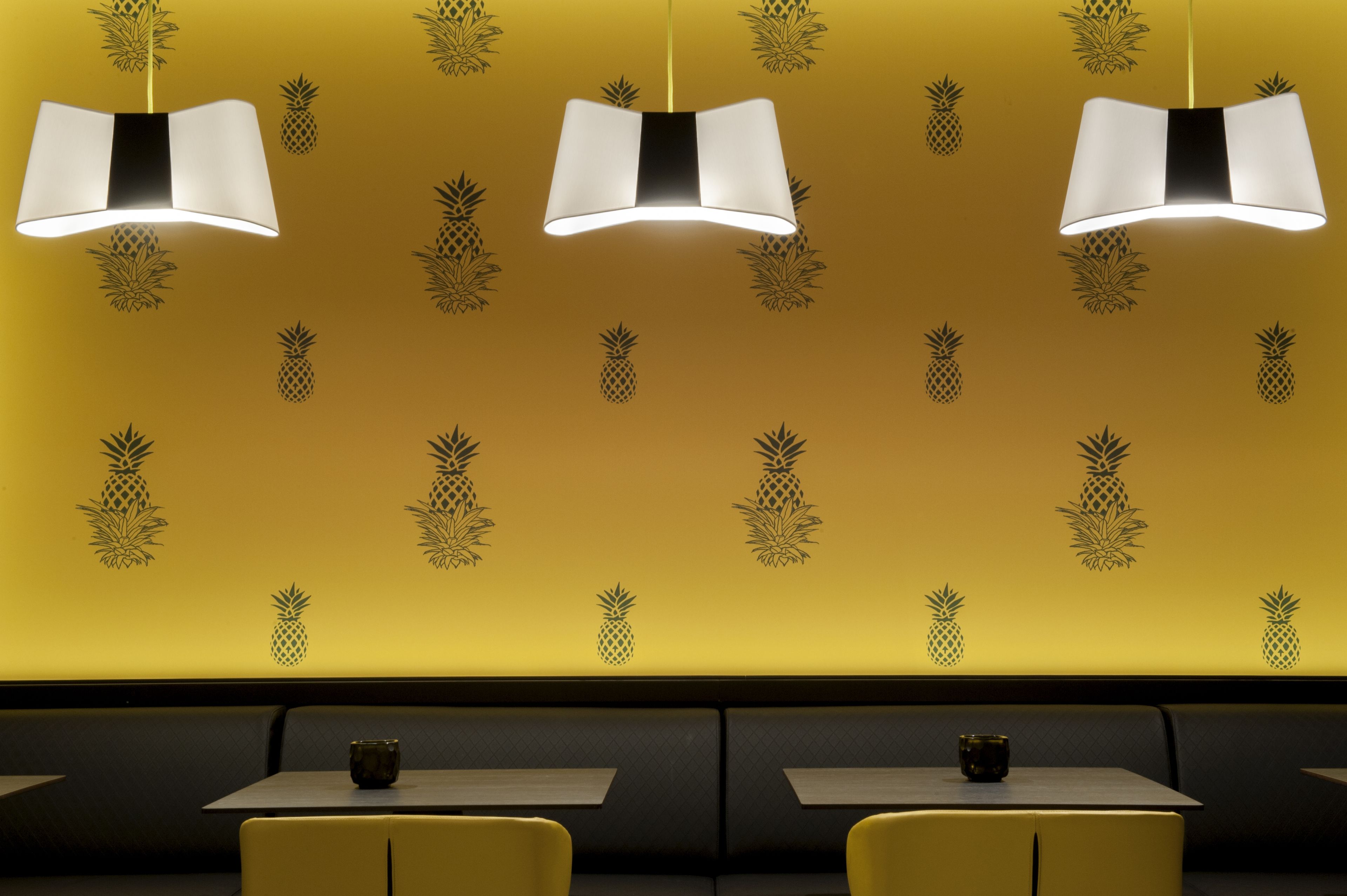 A restaurant interior with yellow walls, pineapple wall decals, and three pendant lights.