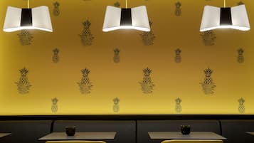 Ein Restaurantinneres mit gelben Wänden, Ananas-Wandbildern und drei Pendelleuchten.