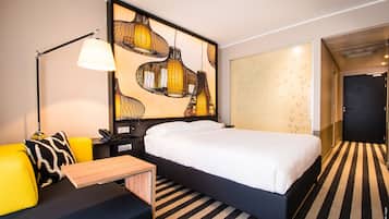 Una camera d'albergo con un letto, una scrivania, una sedia, una lampada e un'ampia opera d'arte appesa al muro.