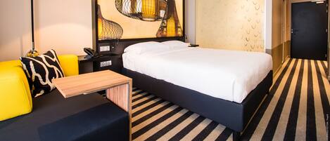 Habitación de hotel con cama, escritorio, silla, lámpara y una obra de arte grande en la pared.