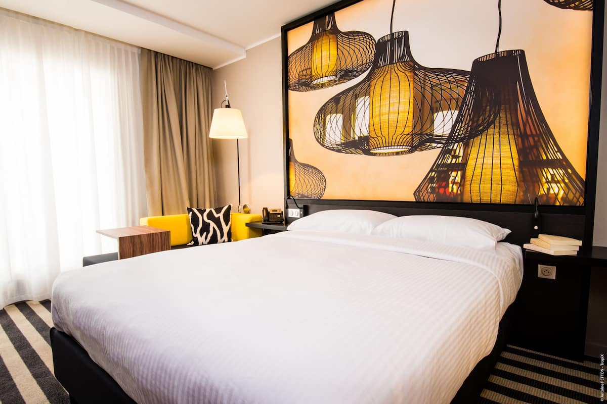 A hotel room with a large bed, a desk with a lamp, and a wall art piece.
