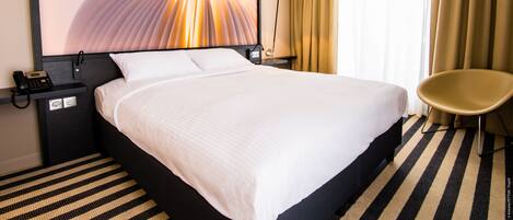 Una habitación de hotel con una cama grande, una silla, una mesita de noche con teléfono y una lámpara de pared.