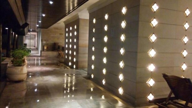 A corridor with reflective flooring, a seating area with a chair, and a wall with illuminated panels. - Baan Sathorn Riverfront (Bangkok)