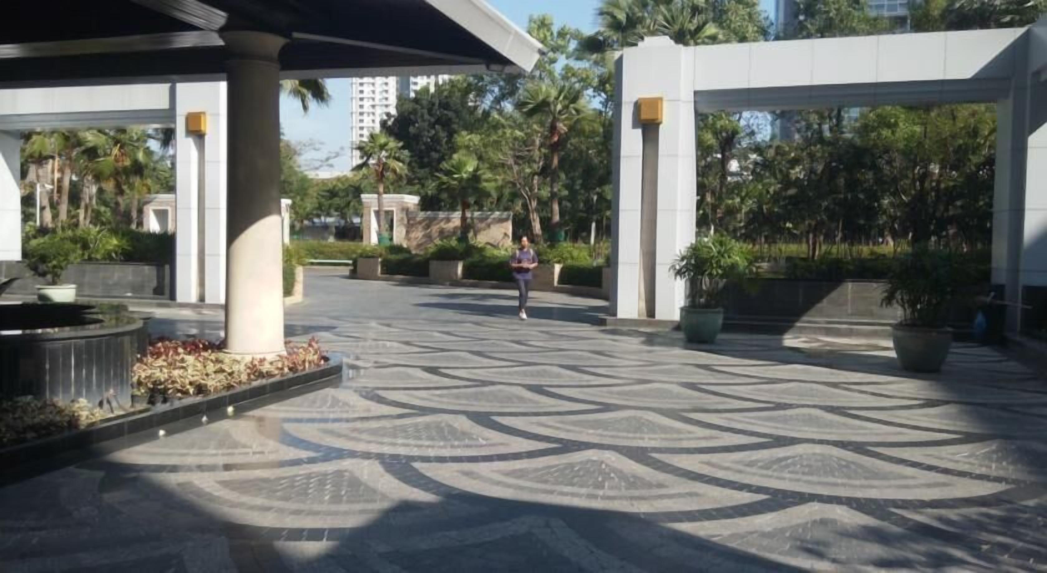 A spacious outdoor area with a patterned floor, large planters, and a covered walkway.