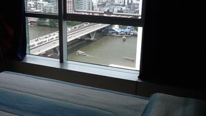 A view from a window overlooking a river with a bridge and buildings in the background. - Baan Sathorn Riverfront (Bangkok)
