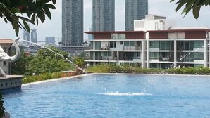 A swimming pool with a water fountain, surrounded by greenery and modern buildings in the background. - Baan Sathorn Riverfront (Bangkok)