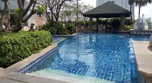 A swimming pool with clear blue water, surrounded by greenery and a gazebo.
