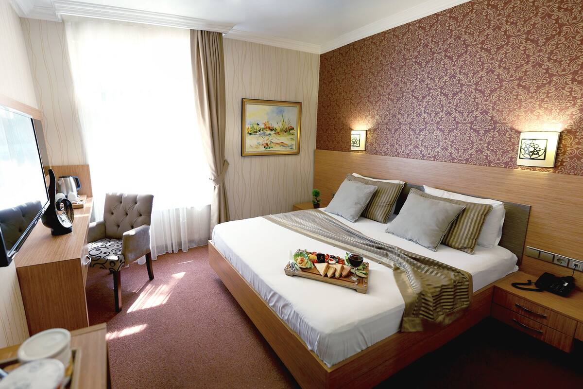 A hotel room with a bed, bedside table, TV, and a painting on the wall.