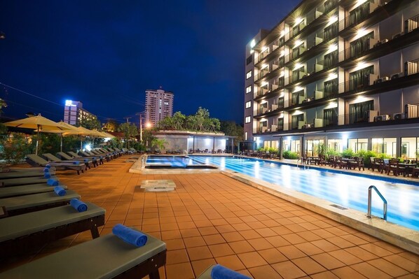 A rooftop pool area with sun loungers and a dining area, surrounded by a modern building with balconies. - Savotel (Sattahip)