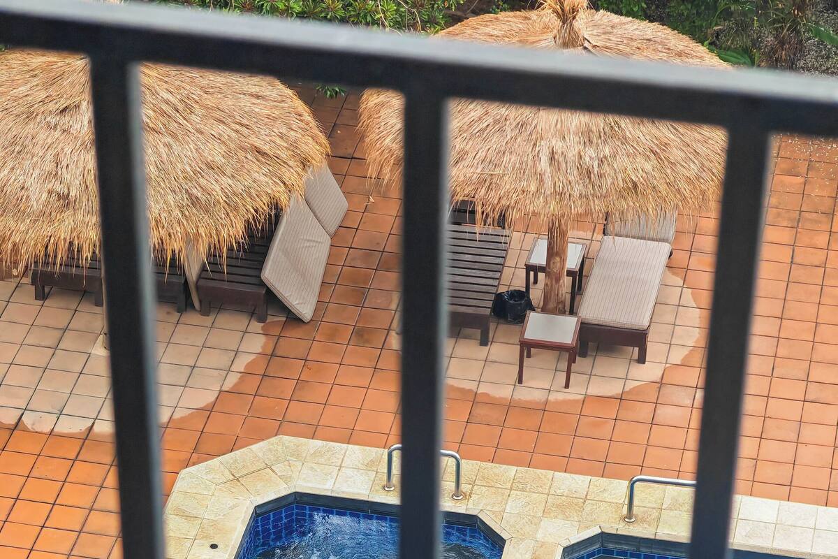 A swimming pool with two hot tubs, surrounded by lounge chairs and thatched umbrellas.