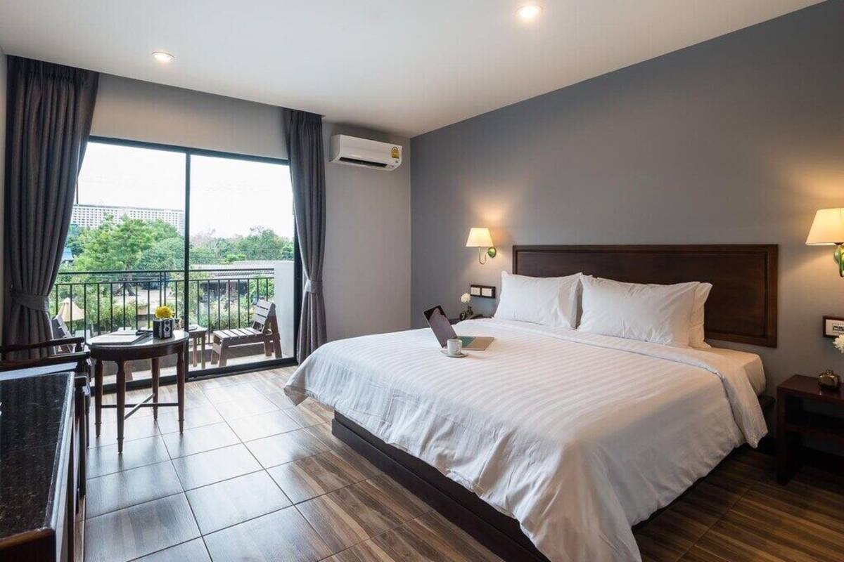 A hotel room with a large bed, a balcony with a table and chairs, and a view of greenery.