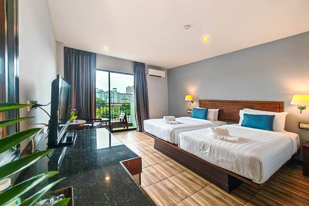A hotel room with two beds, a desk, and a view of buildings.