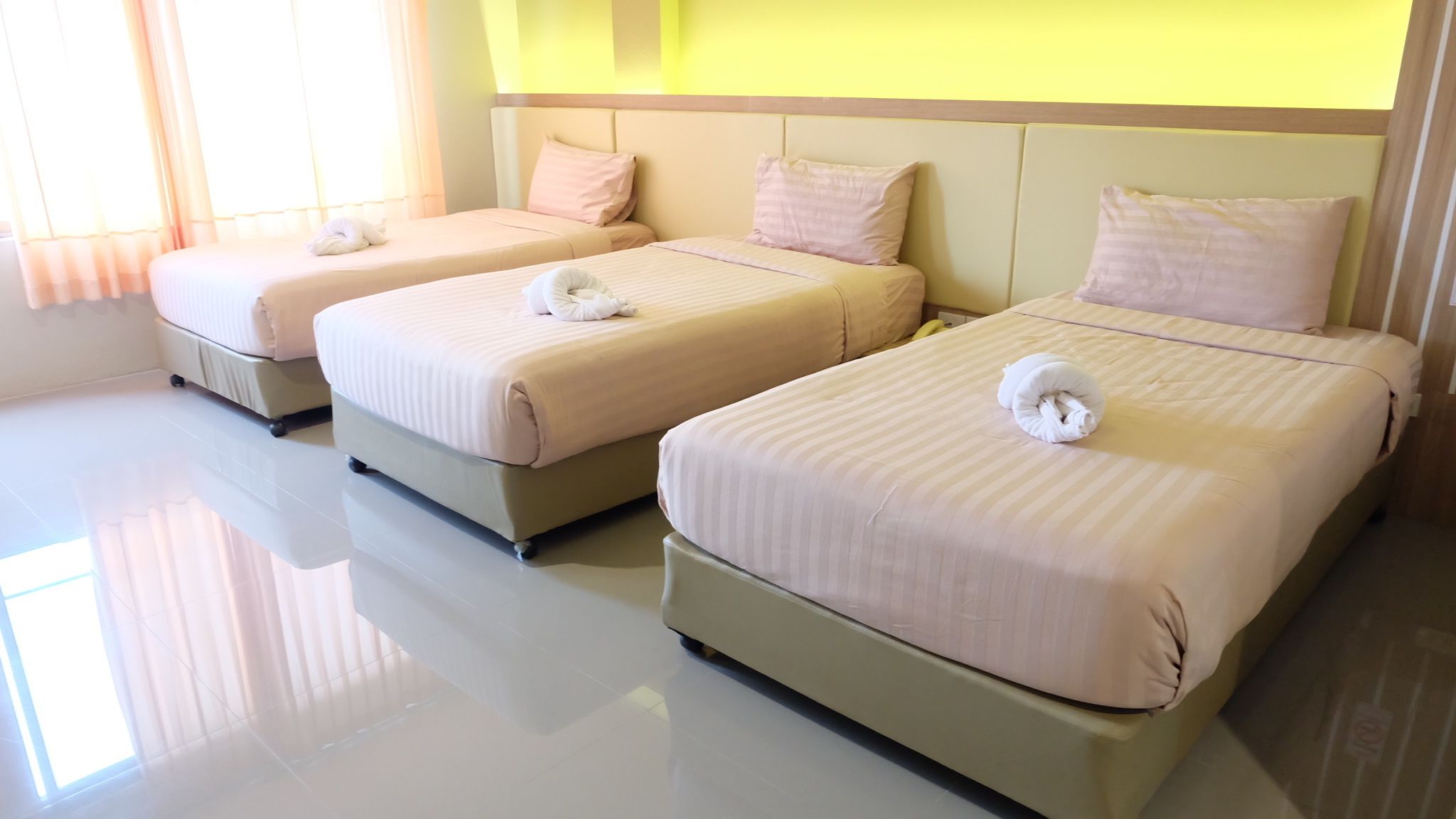 A hotel room with three beds, each with a neatly folded towel.