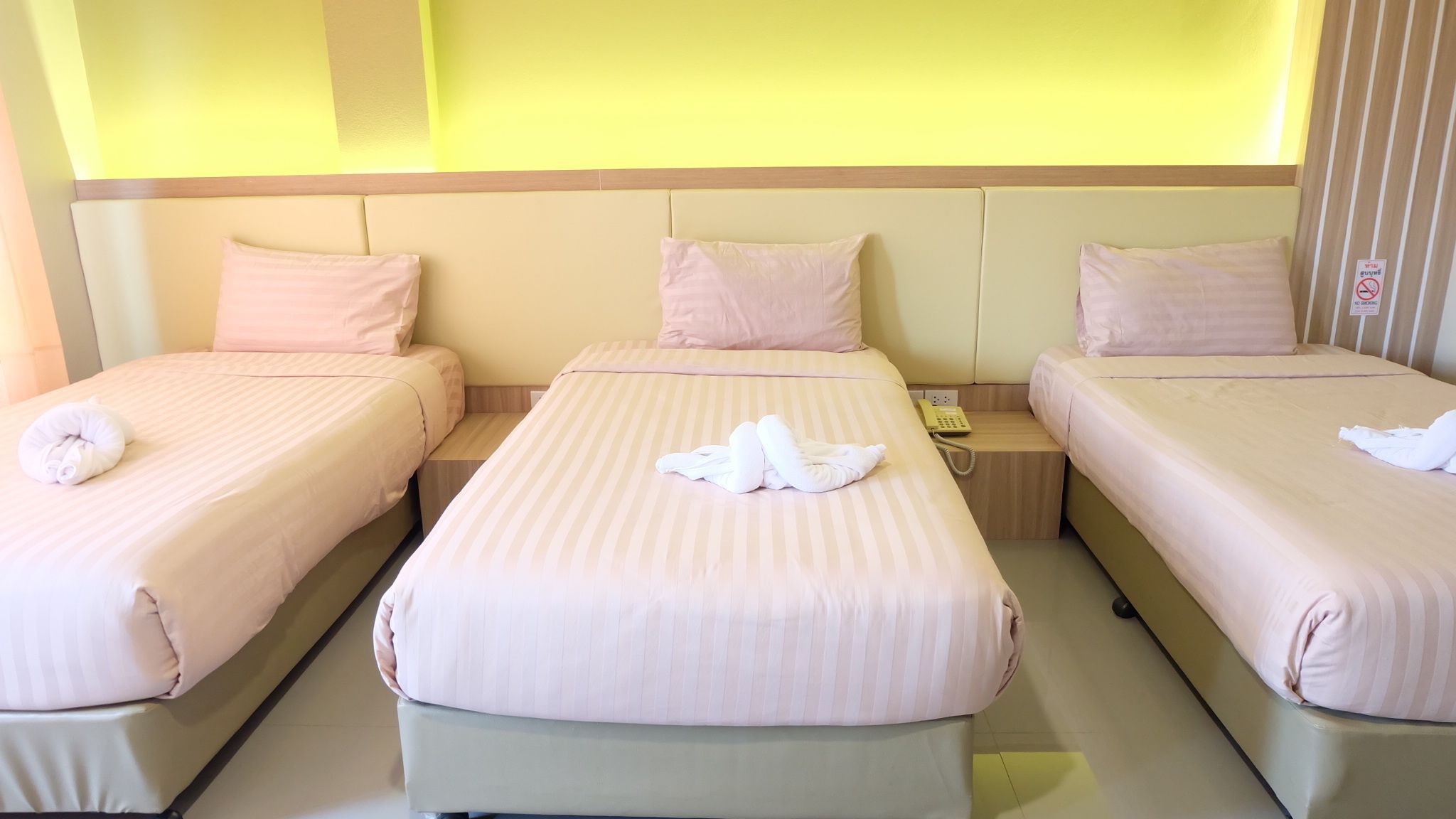 A hotel room with three beds, each with a pillow and a folded towel.