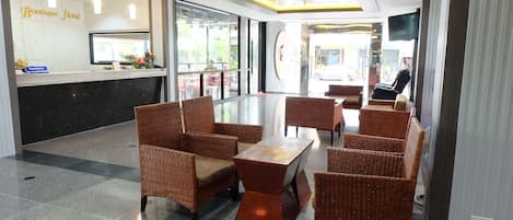 A hotel lobby with wicker furniture, a reception desk, and a large TV screen.