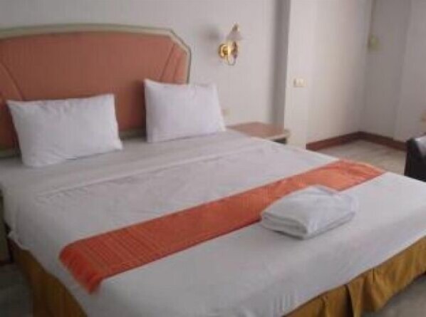 Una cama bien hecha con ropa de cama blanca y naranja, un cabecero de madera y una mesita de noche con una lámpara.