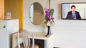A hotel room with a desk, chair, a television displaying a person, a refrigerator, and a vase with flowers. - Silom Boutique Hotel Hatyai (Hat Yai)