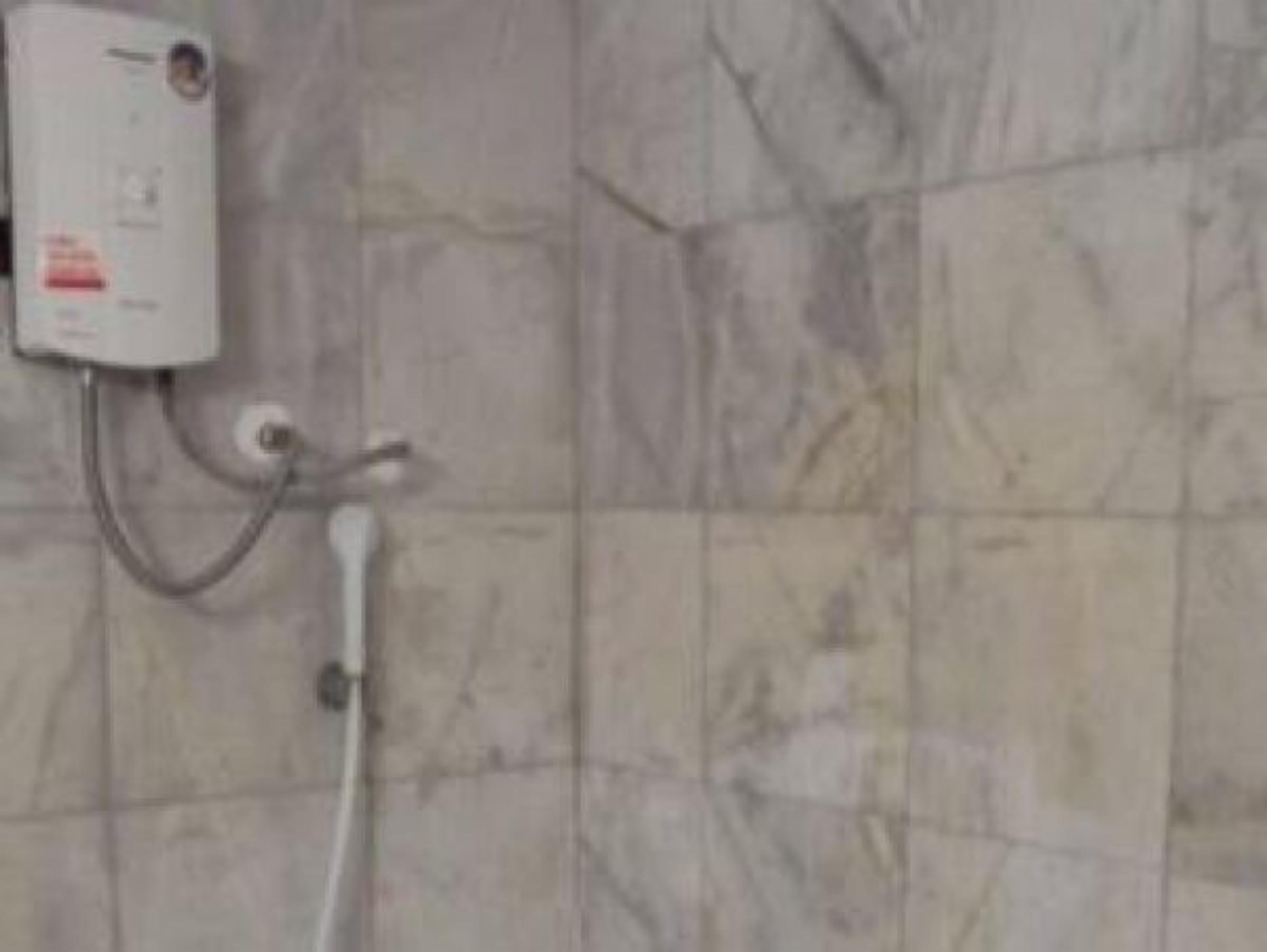 Un baño con pared de azulejos blancos, un enchufe blanco y una tubería blanca.