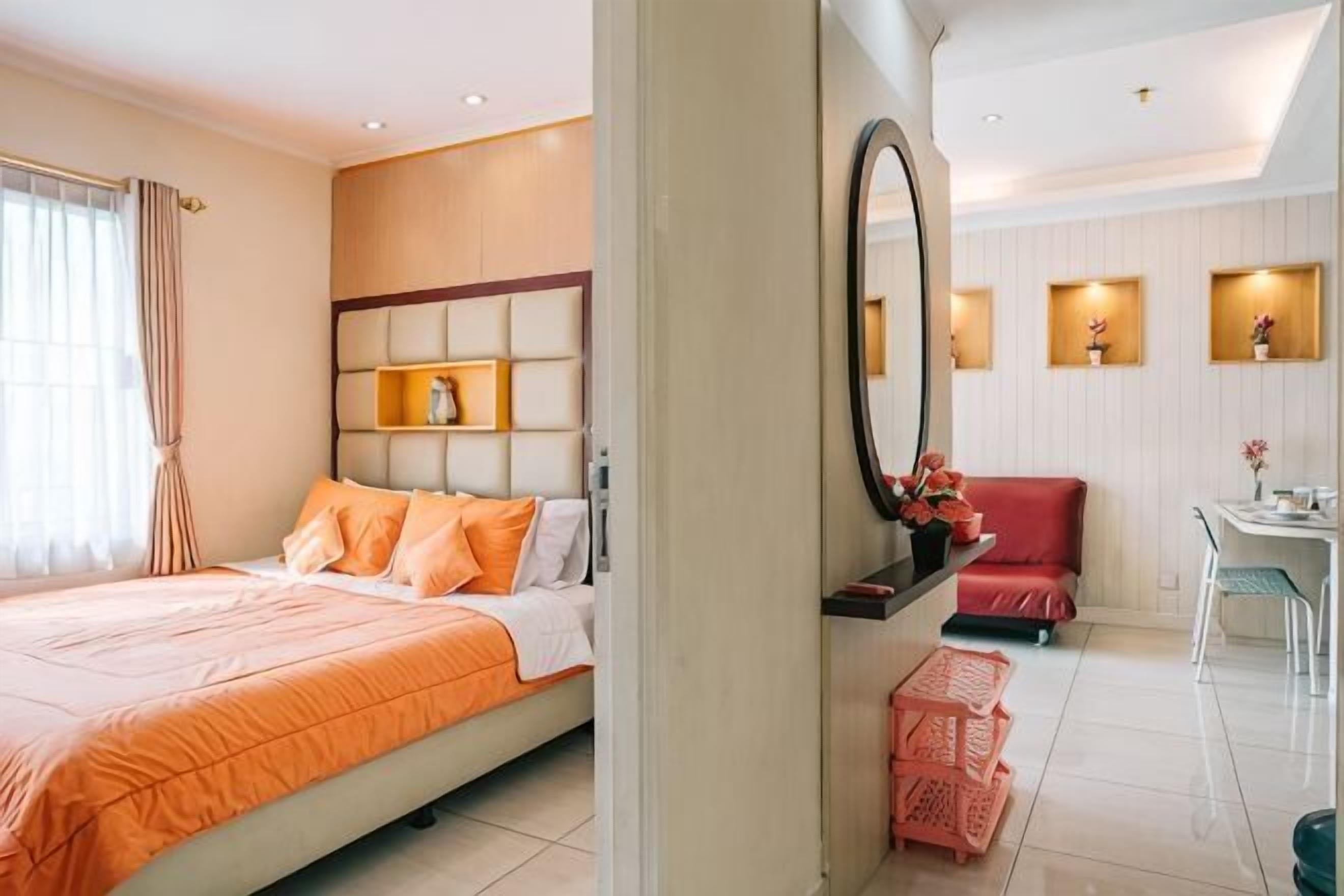 A hotel room with a bed, a desk, a chair, a mirror, and a small table with a vase.