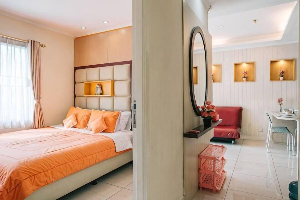 Quarto de hotel com cama, escrivaninha, cadeira, espelho e uma pequena mesa com um vaso.