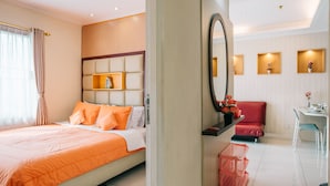 A hotel room with a bed, a desk, a chair, a mirror, and a small table with a vase of flowers.