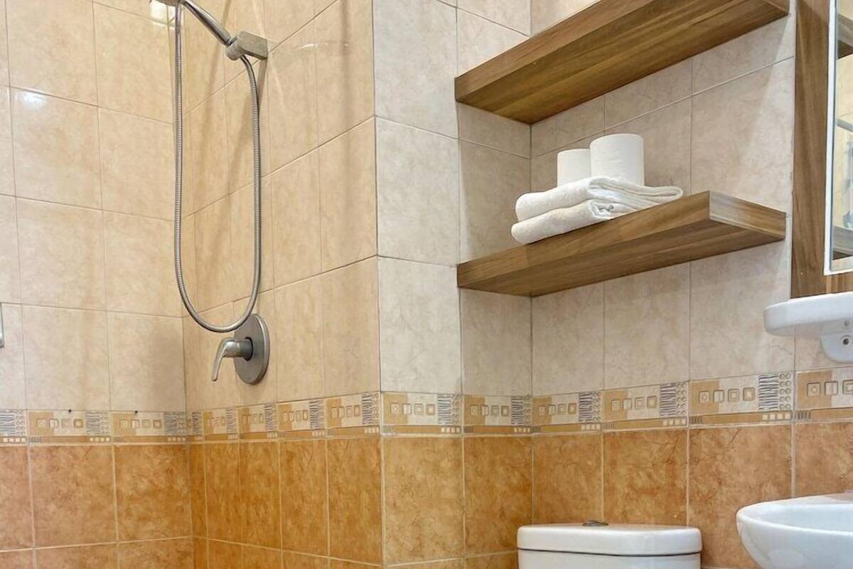 Casa de banho com sanita, chuveiro e um armário com produtos de higiene.