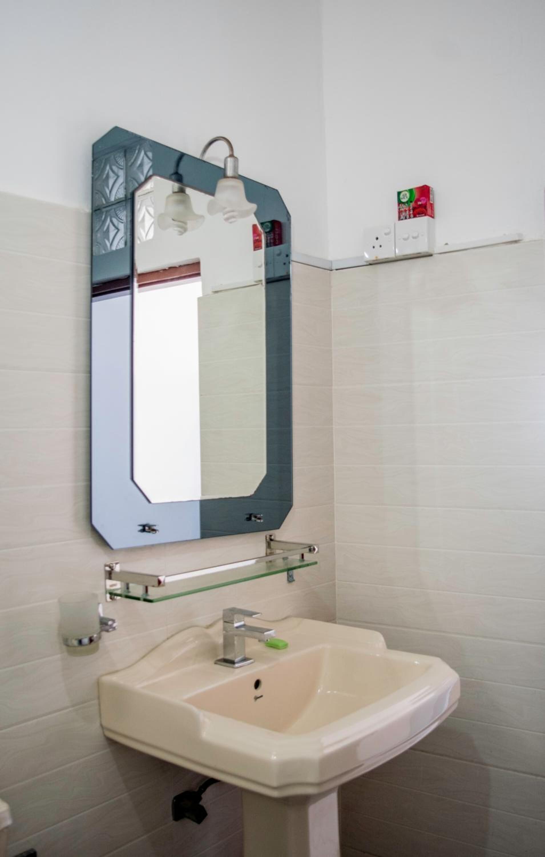 Un baño con lavamanos blanco, un espejo de marco geométrico y un estante con artículos de tocador.