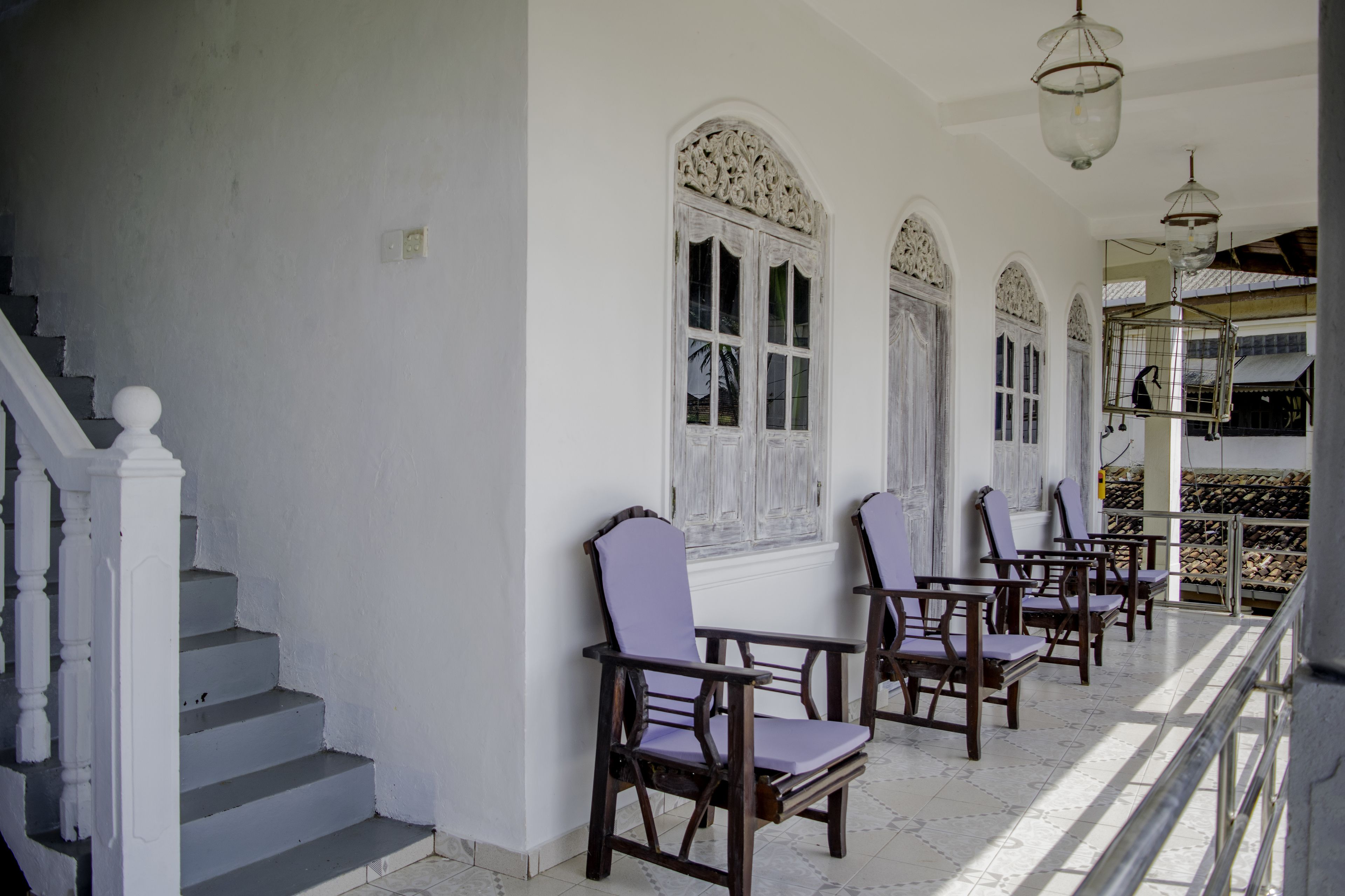 A staircase with white balustrades leading to a landing with a row of wooden chairs and a birdcage.