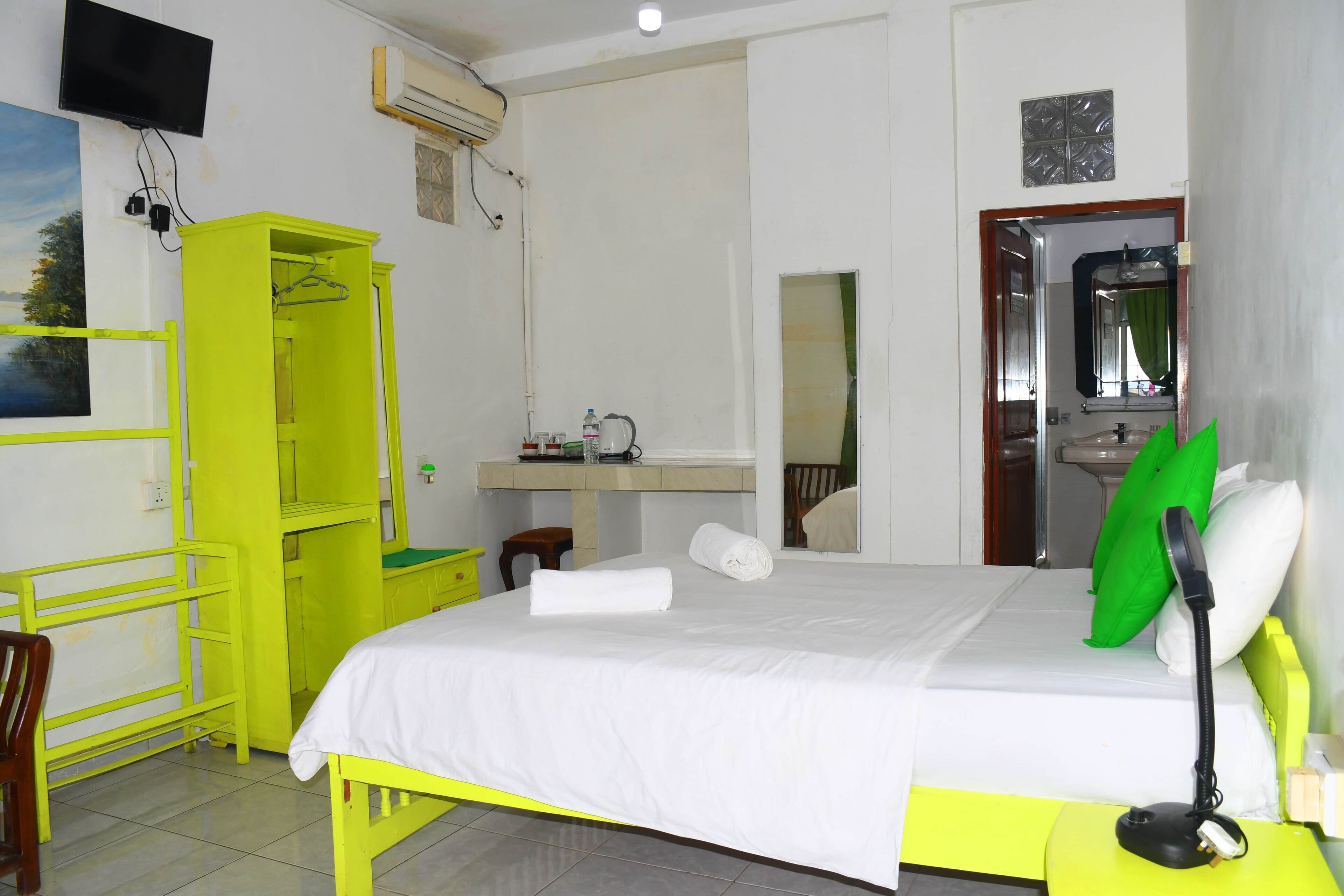 A hotel room with a bed, a desk, a chair, a wardrobe, and a mirror.