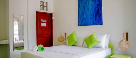 A bed with green and white bedding, a red door, a blue abstract painting, and a small green nightstand with a phone.