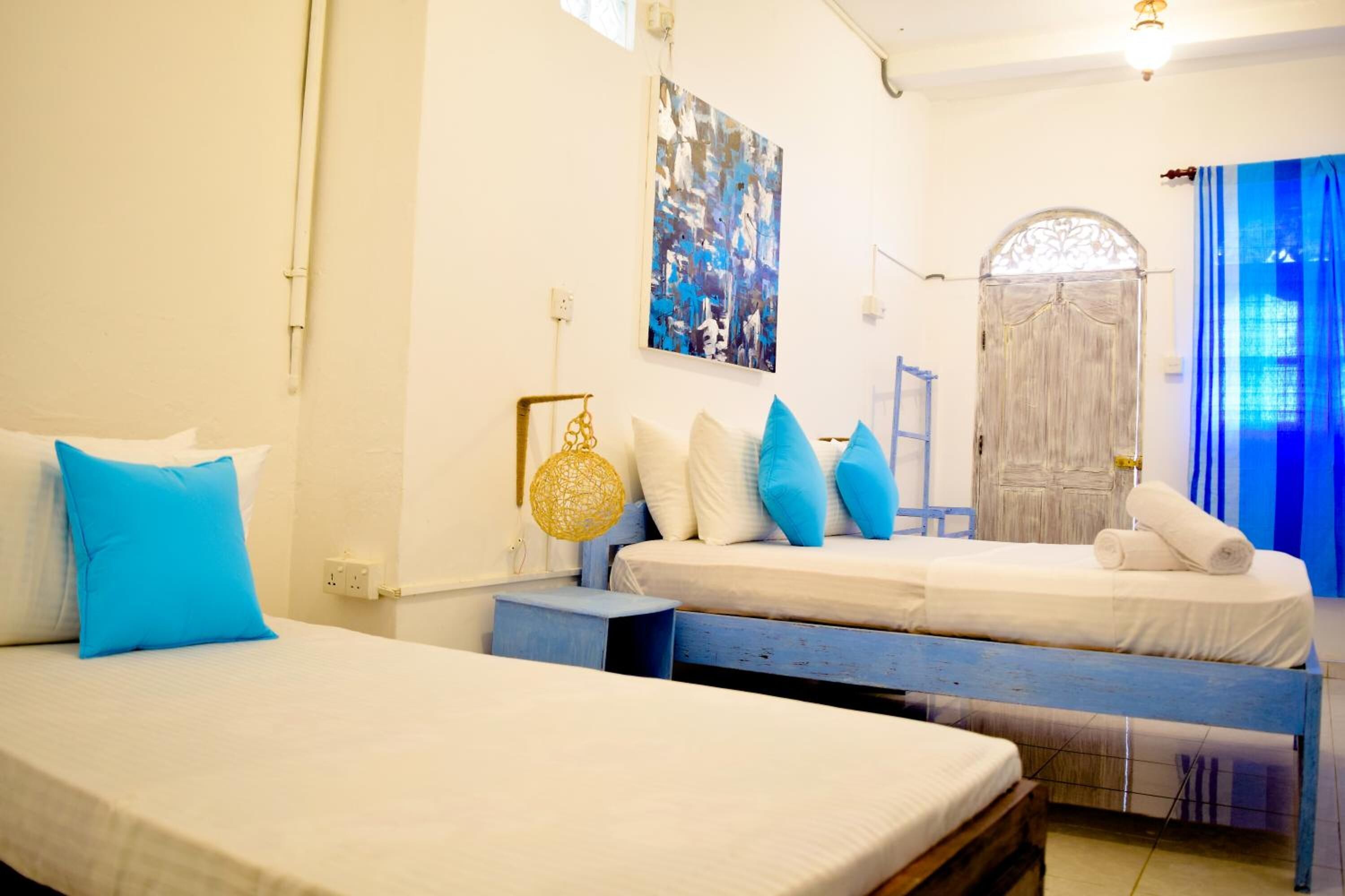 Una habitación con dos camas, una cortina azul, una puerta blanca y una obra de arte colgada en la pared.