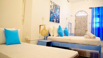 Una habitación con dos camas, una cortina azul, una puerta blanca y una obra de arte colgada en la pared.
