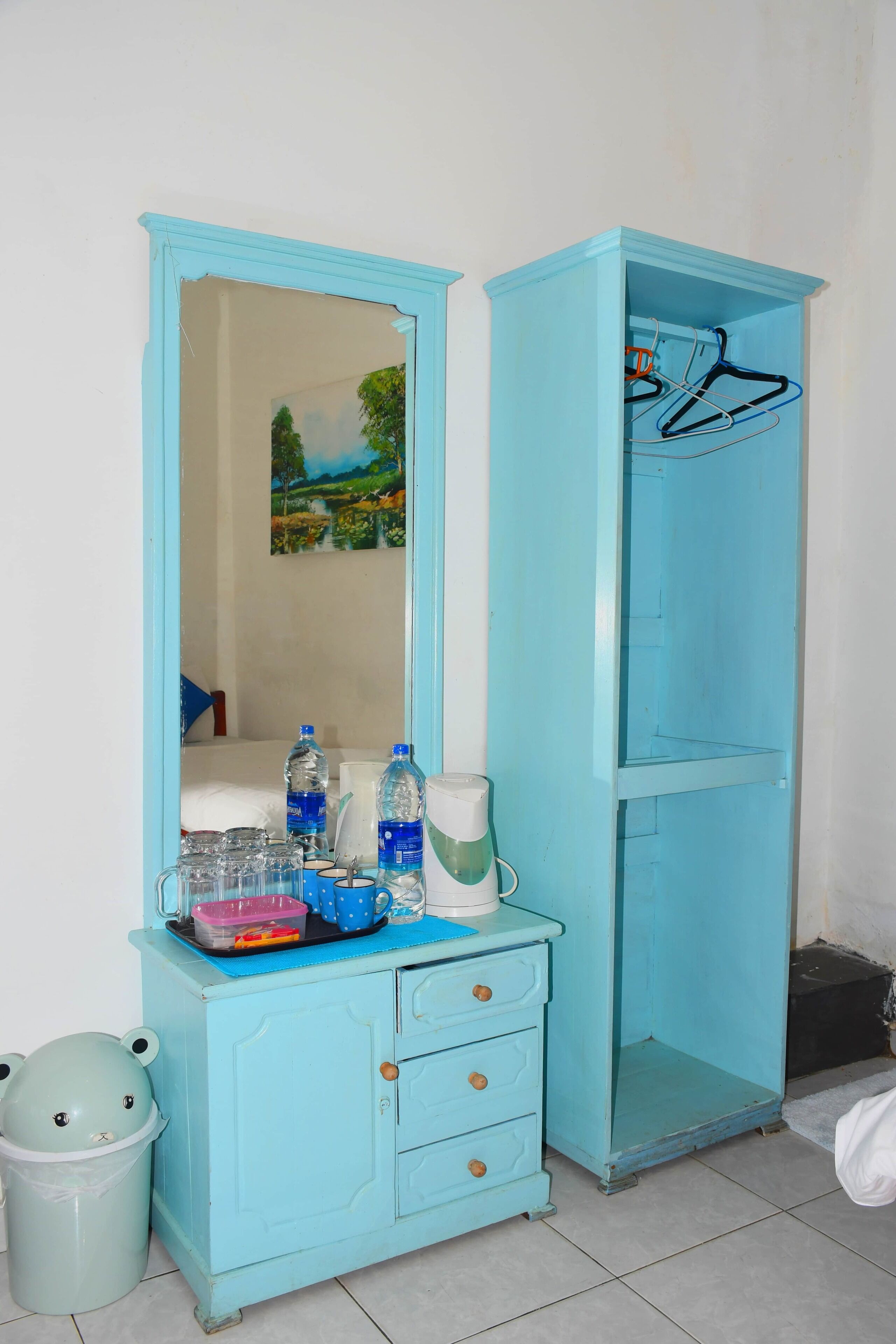 A room with a light blue wardrobe, a mirror, and a small desk with various items.