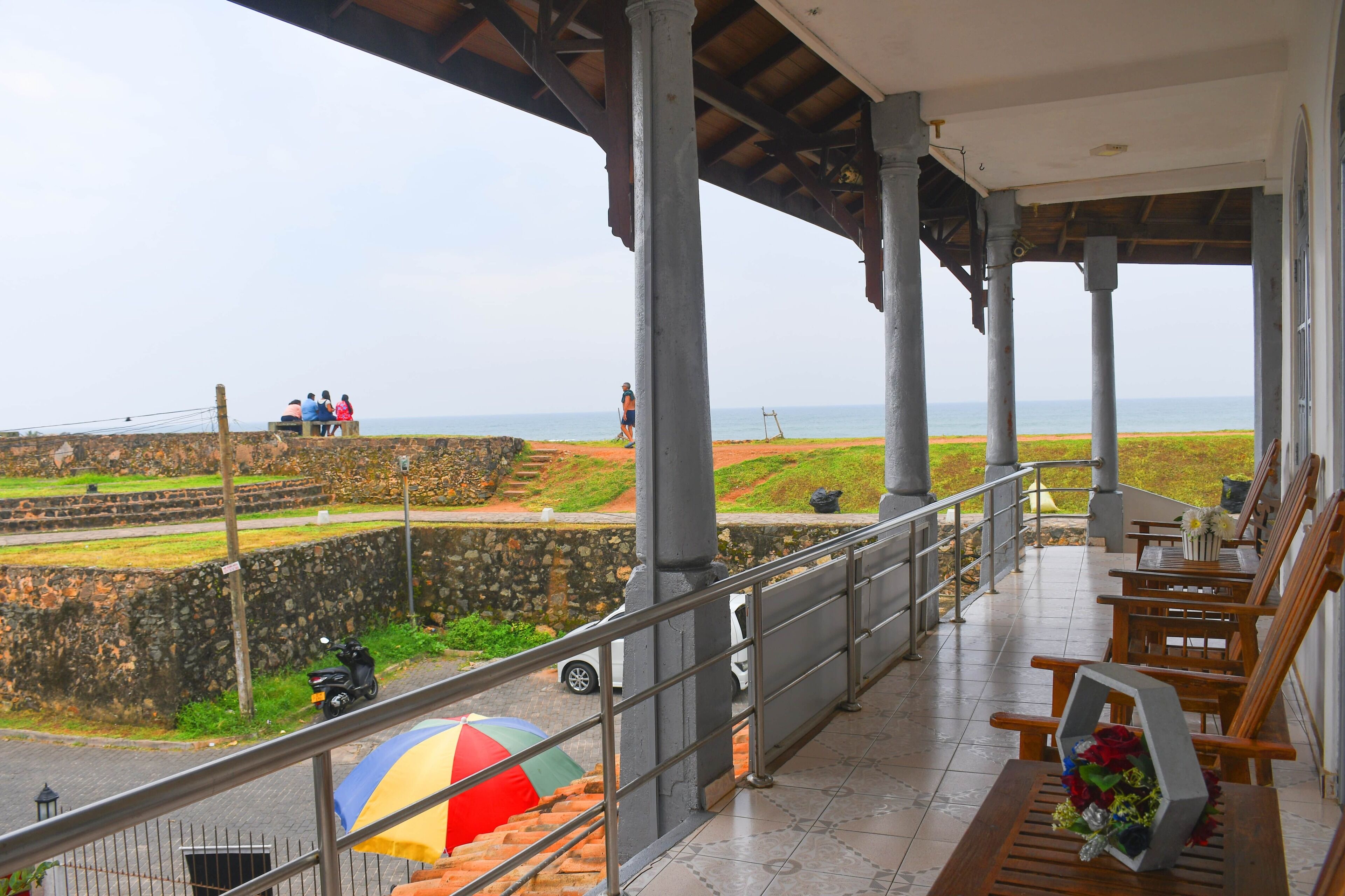 A covered balcony with a view of the sea, stone walls, and a parked scooter.