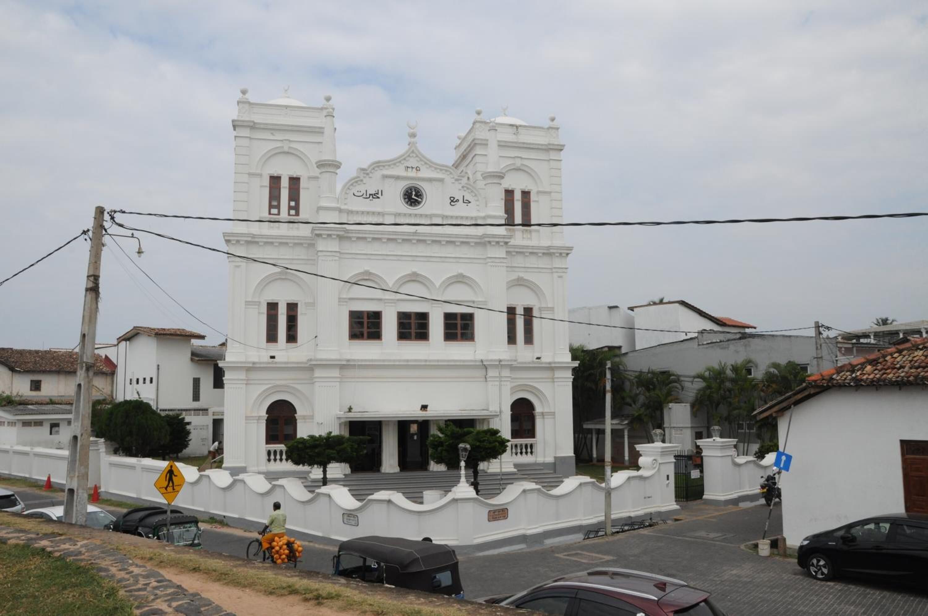 Un edificio de estilo colonial blanco con una torre de reloj, ventanas en arco y una entrada central.