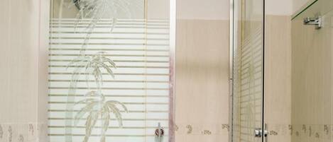 A glass-enclosed shower stall with a white floor, a glass door, and a showerhead.