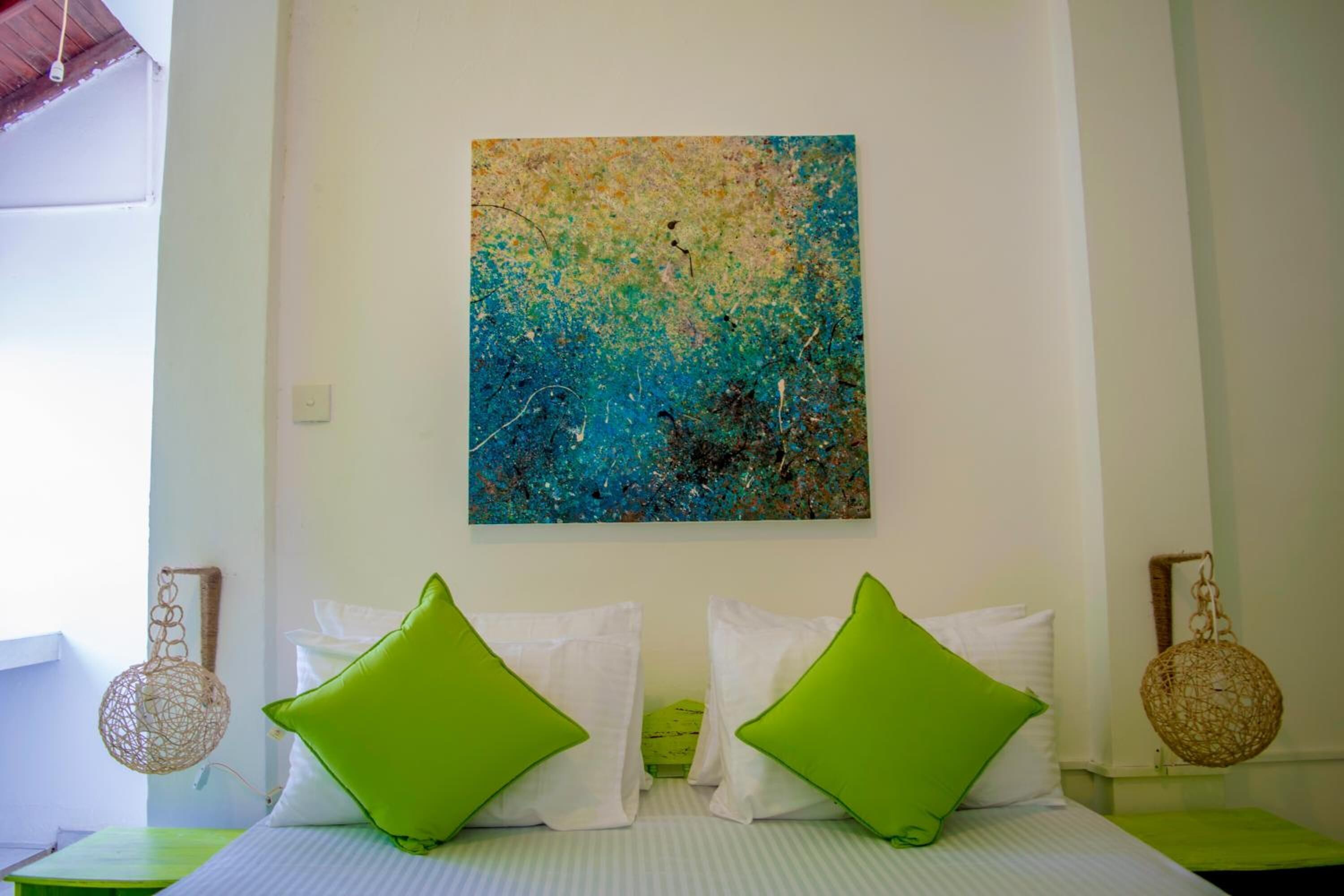 Um quarto com uma cama, travesseiros verdes, um candeeiro pendente e um quadro na parede.