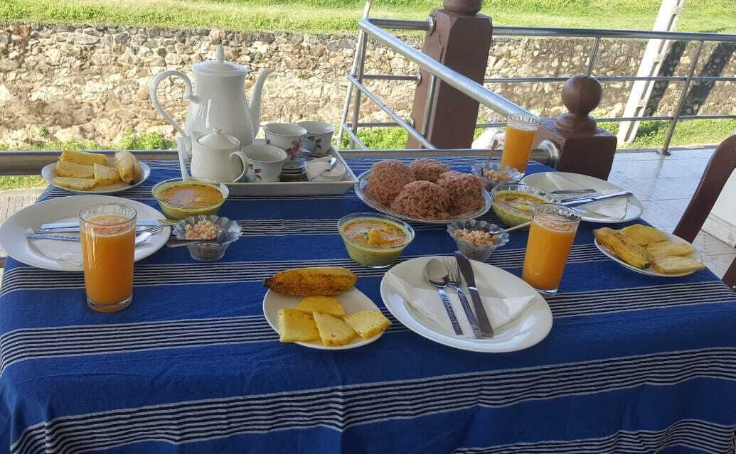 A breakfast table set outdoors with a variety of dishes, including bread, eggs, and fruit, along with cups and a pitcher.