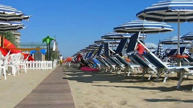 Una playa con filas de tumbonas y sombrillas a rayas.