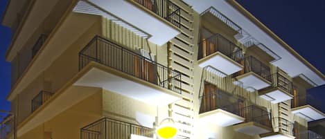 A multi-story hotel with balconies, outdoor seating, and a well-lit entrance.