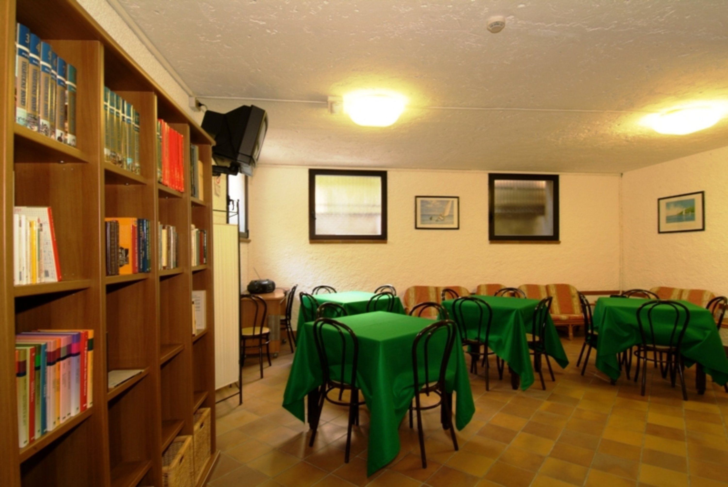 A room with multiple tables covered in green tablecloths, wooden bookshelves filled with books, and framed pictures on the walls.