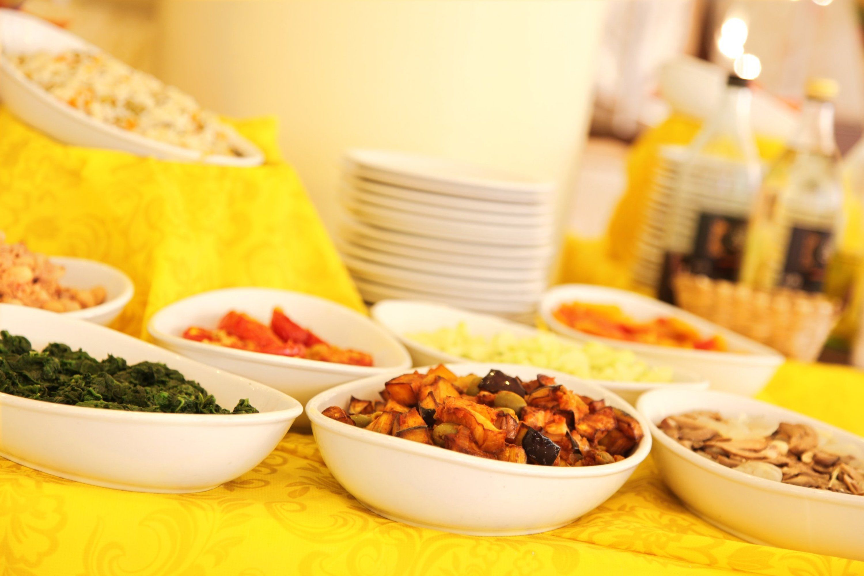 A table with various dishes in bowls, a stack of plates, and bottles of beverages.