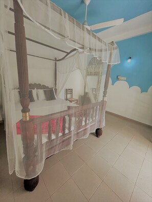 Un lit à baldaquin à quatre poteaux, un ventilateur de plafond et un mur orné d’une fresque représentant des nuages.