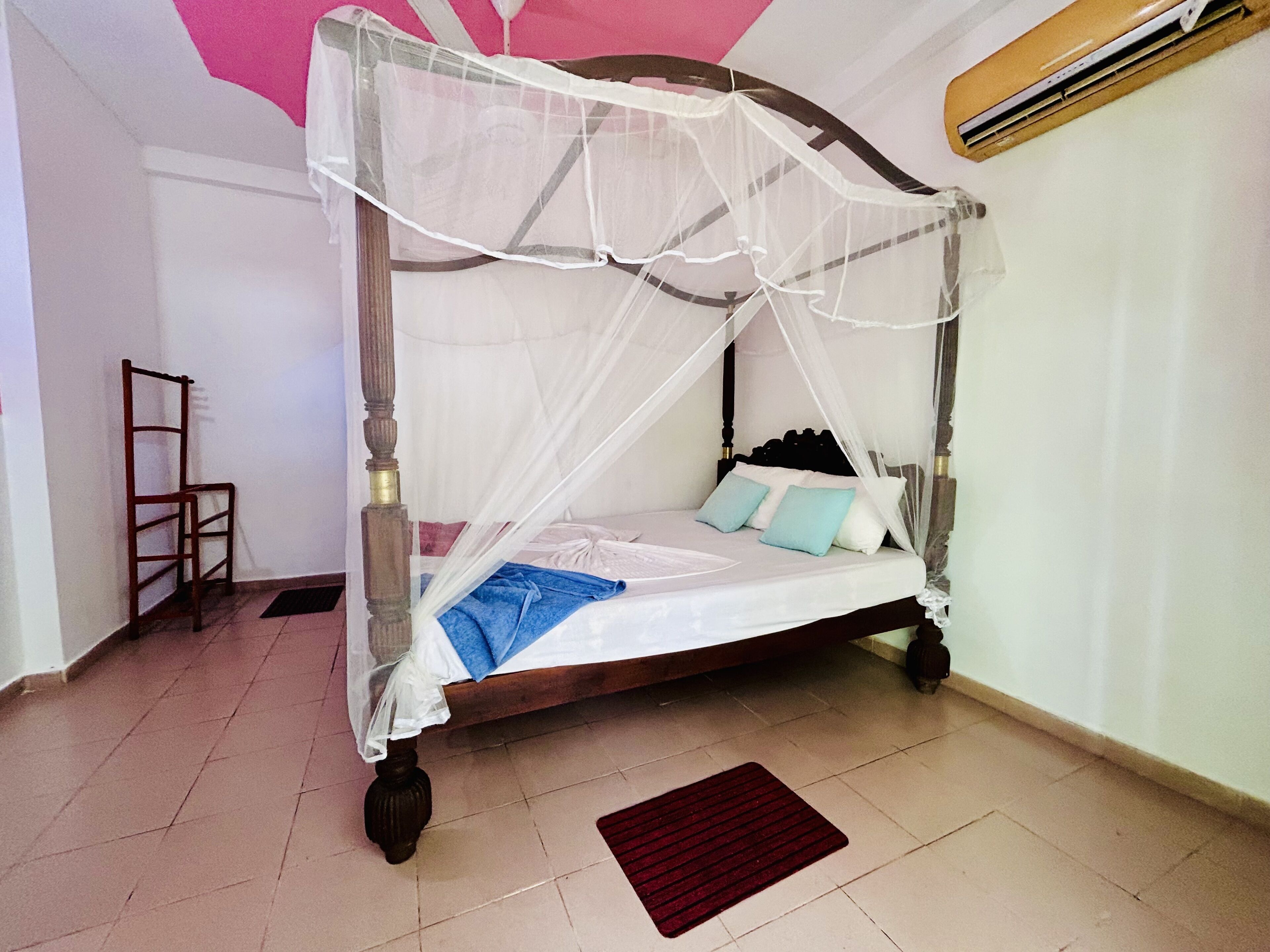 A four-poster bed with a canopy, a wooden chair, and a red mat on the floor.