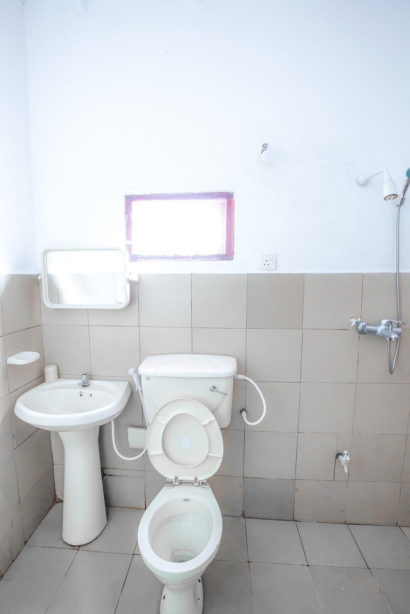 Et lille badeværelse med toilet, håndvask og bruser.