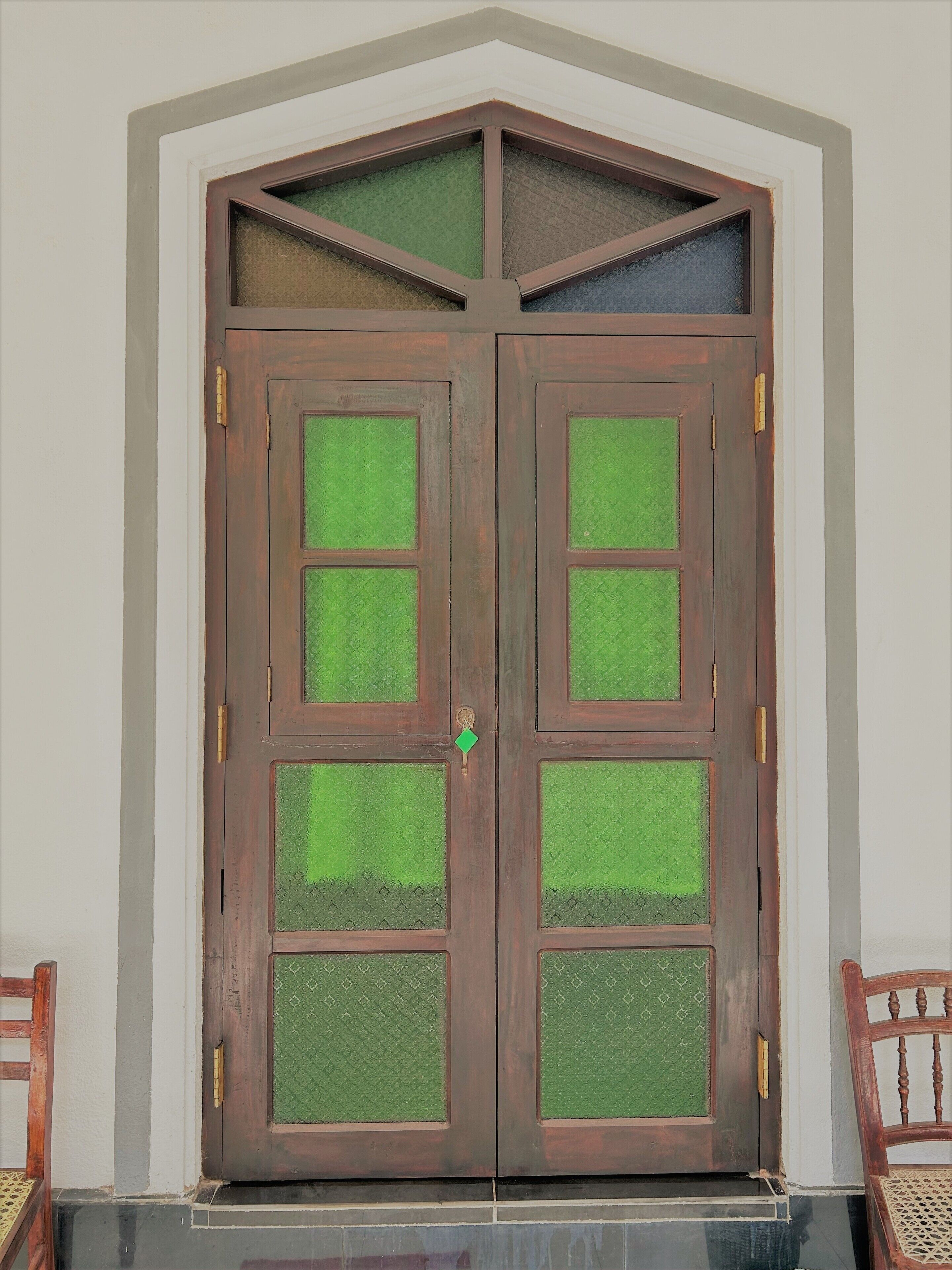 A double wooden door with green textured glass panels and a brass handle.