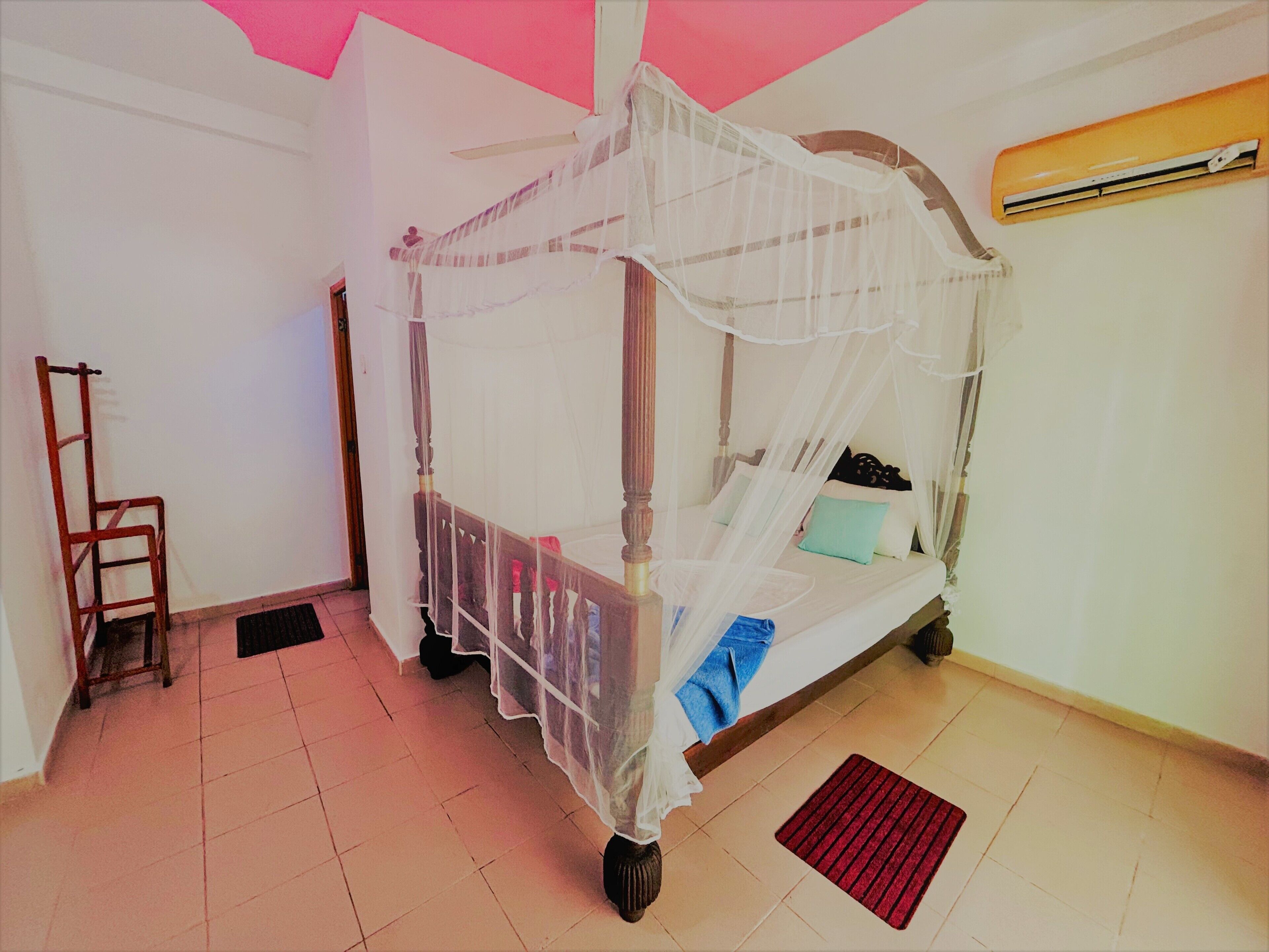 Een kamer met een hemelbed, een ladder, een rode mat en een airconditioning.
